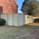 A wooden fence constructed from vertical planks, showcasing a natural wood finish, sturdy design, and surrounding yard filled with brown and green grass.