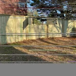 A wooden fence constructed from vertical planks, showcasing a natural wood finish, sturdy design, and surrounding yard filled with brown and green grass.