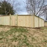 A wooden fence constructed from vertical planks, showcasing a natural wood finish, sturdy design, and surrounding yard filled with yellow grass.