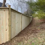 A wooden fence constructed from vertical planks, showcasing a natural wood finish, sturdy design, and surrounding yard filled with yellow grass.