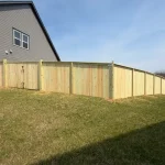 A wooden fence constructed from vertical planks, showcasing a natural wood finish, sturdy design, and surrounding yard filled with green grass.