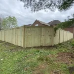 A wooden fence constructed from vertical planks, showcasing a natural wood finish, sturdy design, and surrounding yard filled with green grass.