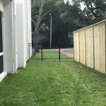 A fence constructed from iron, showcasing a natural wood finish, sturdy design, and surrounding yard filled with green grass.
