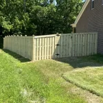 A wooden fence constructed from vertical planks, showcasing a natural wood finish, sturdy design, and surrounding yard filled with green grass.