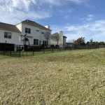 A fence constructed from iron, showcasing a natural wood finish, sturdy design, and two-story home with a surrounding yard filled with green grass.