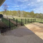 A fence constructed from iron, showcasing a natural wood finish, sturdy design, and surrounding yard filled with green grass.