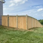 A wooden fence constructed from vertical planks, showcasing a natural wood finish, sturdy design, and surrounding yard filled with green grass.