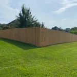 A wooden fence constructed from vertical planks, showcasing a natural wood finish, sturdy design, and surrounding yard filled with green grass.