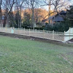A wooden fence constructed from vertical planks, showcasing a natural wood finish, sturdy design, and surrounding yard filled with green grass.