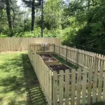 A wooden fence constructed from vertical planks, showcasing a natural wood finish, sturdy design, and surrounding yard filled with green grass.