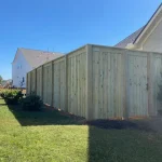 A wooden fence constructed from vertical planks, showcasing a natural wood finish, sturdy design, and surrounding yard filled with green grass.