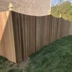 A wooden fence constructed from vertical planks, showcasing a natural wood finish, sturdy design, and surrounding yard filled with green grass.