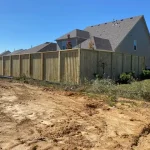 A wooden fence constructed from vertical planks, showcasing a natural wood finish, sturdy design, and surrounding yard filled with dirt.
