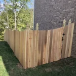 A wooden fence constructed from vertical planks, showcasing a natural wood finish, sturdy design, and surrounding yard filled with green grass.