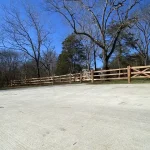 A farm wooden fence constructed from vertical planks, showcasing a natural wood finish and sturdy design, and a concrete driveway.
