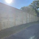 A wooden fence constructed from vertical planks, showcasing a natural wood finish, sturdy design, and surrounding yard filled with green grass.