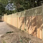 A wooden fence constructed from vertical planks, showcasing a natural wood finish, sturdy design, and surrounding yard filled with dirt.