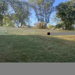 A wooden fence constructed from vertical planks, showcasing a natural wood finish, sturdy design, and surrounding yard filled with green grass.