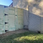 A wooden fence and gate constructed from vertical planks, showcasing a natural wood finish, sturdy design, and surrounding yard filled with green grass.