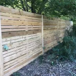 A wooden fence constructed from vertical planks, showcasing a natural wood finish, sturdy design, and surrounding yard filled with green grass.