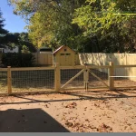 A farm wooden fence constructed from vertical planks, showcasing a natural wood finish and sturdy design, and metal meshing.