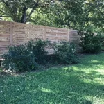 A wooden fence constructed from vertical planks, showcasing a natural wood finish, sturdy design, and surrounding yard filled with green grass.