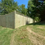 A wooden fence constructed from vertical planks, showcasing a natural wood finish, sturdy design, and surrounding yard filled with green grass.