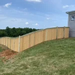 A wooden fence constructed from vertical planks, showcasing a natural wood finish, sturdy design, and surrounding yard filled with green grass.
