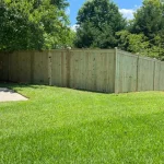 A wooden fence constructed from vertical planks, showcasing a natural wood finish, sturdy design, and surrounding yard filled with green grass.