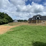A farm wooden fence constructed from vertical planks, showcasing a natural wood finish and sturdy design, and a big barn in the background.