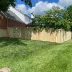 A wooden fence constructed from vertical planks, showcasing a natural wood finish, sturdy design, and surrounding yard filled with green grass.