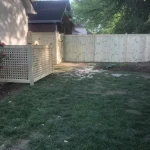 A wooden fence constructed from vertical planks, showcasing a natural wood finish, sturdy design, and surrounding yard filled with green grass.