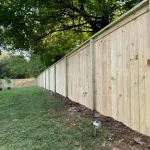 A wooden fence constructed from vertical planks, showcasing a natural wood finish, sturdy design, and surrounding yard filled with green grass.