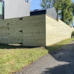 A wooden fence and gate constructed from vertical planks, showcasing a natural wood finish, sturdy design, and surrounding yard filled with green grass.