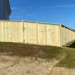 A wooden fence constructed from vertical planks, showcasing a natural wood finish, sturdy design, and surrounding yard filled with brown and green grass.