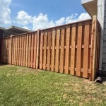 A wooden fence constructed from vertical planks, showcasing a natural wood finish, sturdy design, and surrounding yard filled with green grass.
