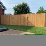 A wooden fence constructed from vertical planks, showcasing a natural wood finish, sturdy design, and surrounding yard filled with green grass.