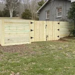 A wooden fence and gate constructed from vertical planks, showcasing a natural wood finish, sturdy design, and surrounding yard filled with green grass.