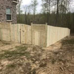 A wooden fence and gate constructed from vertical planks, showcasing a natural wood finish, sturdy design, and surrounding yard filled with brown and green grass.