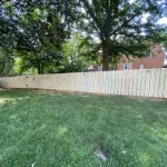 A wooden fence constructed from vertical planks, showcasing a natural wood finish, sturdy design, and surrounding yard filled with green grass.