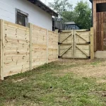 A wooden fence and gate constructed from vertical planks, showcasing a natural wood finish, sturdy design, and surrounding yard filled with green grass.