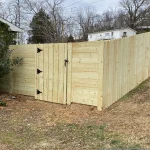 A wooden fence and gate constructed from vertical planks, showcasing a natural wood finish, sturdy design, and surrounding yard filled with brown and green grass.