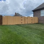 A wooden fence and gate constructed from vertical planks, showcasing a natural wood finish, sturdy design, and surrounding yard filled with green grass.