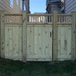 A wooden fence and gate constructed from vertical planks, showcasing a natural wood finish, sturdy design, and surrounding yard filled with green grass.