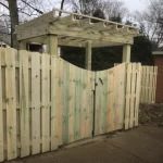 A wooden fence and gate constructed from vertical planks, showcasing a natural wood finish, sturdy design, and surrounding yard filled with dirt.