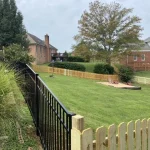 A fence constructed from iron, showcasing a natural wood finish, sturdy design, and surrounding yard filled with green grass.