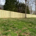 A wooden fence constructed from vertical planks, showcasing a natural wood finish, sturdy design, and surrounding yard filled with green grass.