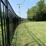 A fence constructed from iron, showcasing a natural wood finish, sturdy design, and surrounding yard filled with green grass.
