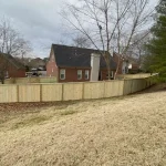 A wooden fence constructed from vertical planks, showcasing a natural wood finish, sturdy design, and surrounding yard filled with yellow grass.