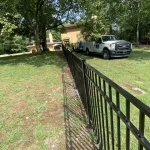 A fence constructed from iron, showcasing a natural wood finish, sturdy design, and surrounding yard filled with green grass.